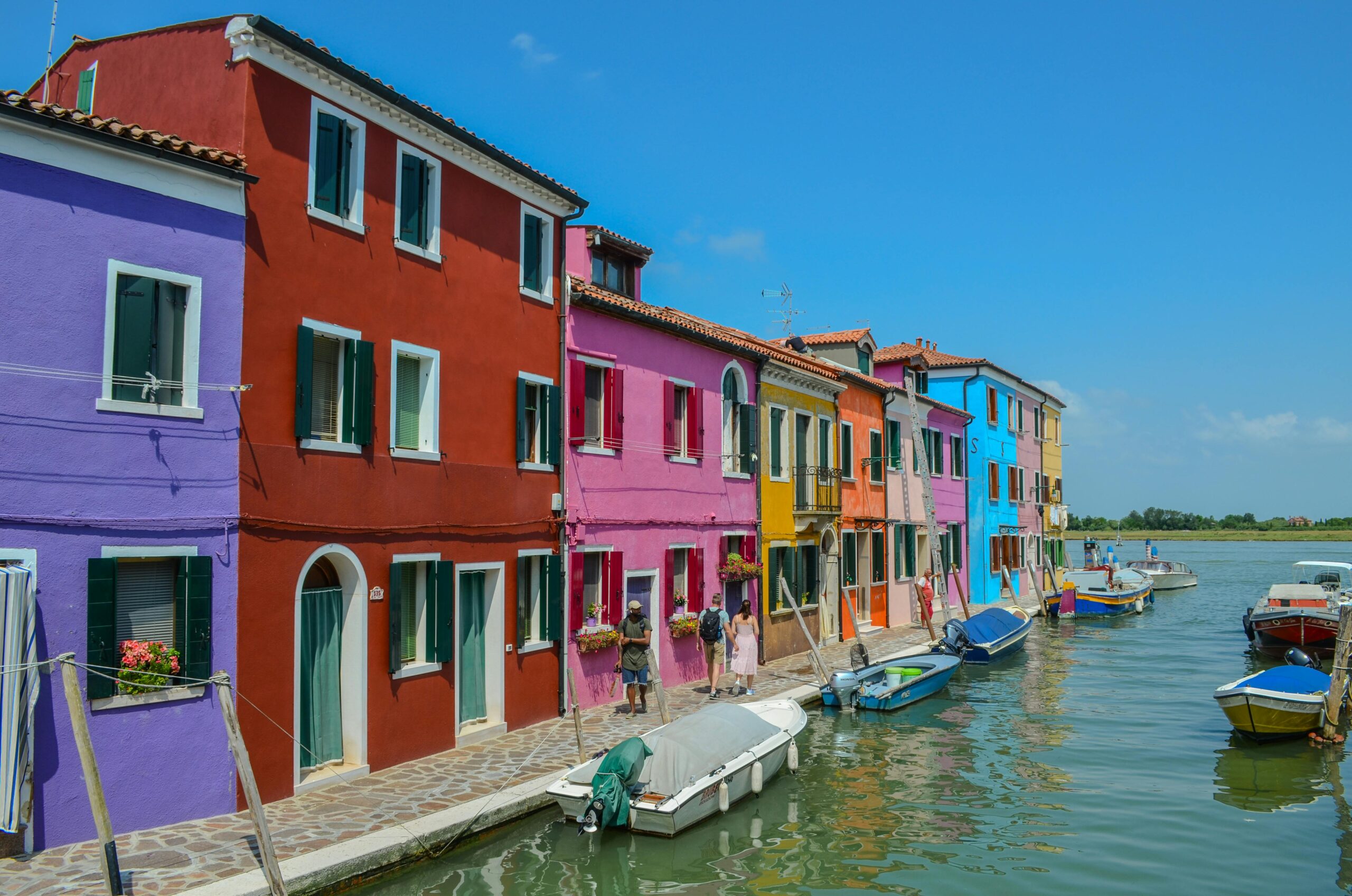 Vibrant multi-colored houses line a canal in Burano, Venice, Italy, capturing its iconic architecture.